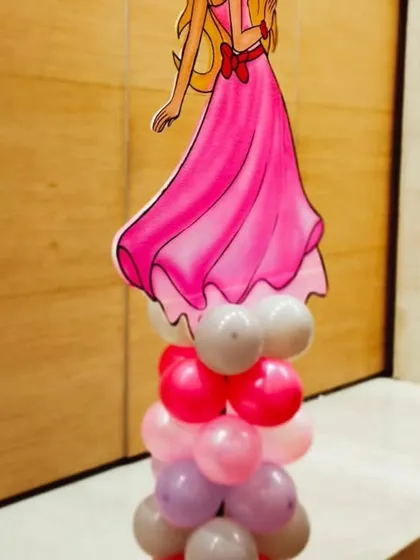 A Barbie cutout on a multi-colored balloon pillar, used as a decorative element for a theme party.