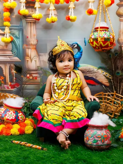 A full view of a little Radha in her festive attire, sitting on a miniature chair in the beautiful Janmashtami setup.