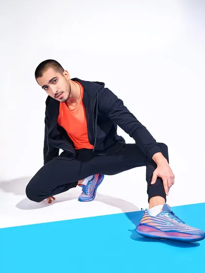 A clean, minimalist setup for a shoe lookbook. The model's crouching pose against a two-tone background draws the eye directly to the colorful sneakers, highlighting their unique design for e-commerce.