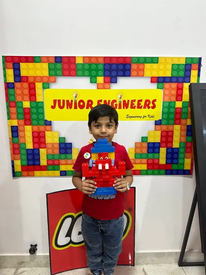 A young boy stands in front of our Junior Engineers branded backdrop, holding his red and blue LEGO Ganesha.