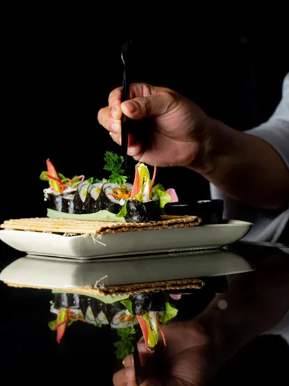 Our sushi menu is a culinary mosaic designed for every palate. Here, a chef adds the final touches to a vegetarian maki roll, crafted to enchant your senses.