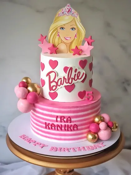 A Barbie-themed whipped cream cake for twins Ira and Kanika. This two-tier cake is all about pink, with hearts, stripes, and a Barbie topper.
