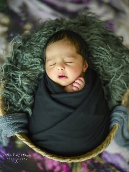 A striking contrast with a dark theme. This baby is wrapped in a black swaddle, resting on a grey fur inside a basket against a floral backdrop, creating a moody and artistic look.