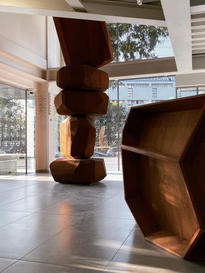 The custom-designed reception desk and a large-scale sculpture in the lobby of the Museum of Art and Photography (MAP). The faceted wooden forms of the furniture echo the geometric language of the building's facade.