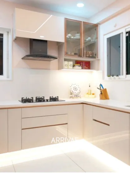 An elegant and bright L-shaped kitchen in a timeless beige finish. This design features a combination of solid and glass-front upper cabinets, sleek handleless drawers, and integrated under-cabinet lighting that creates a warm, inviting, and highly efficient workspace.