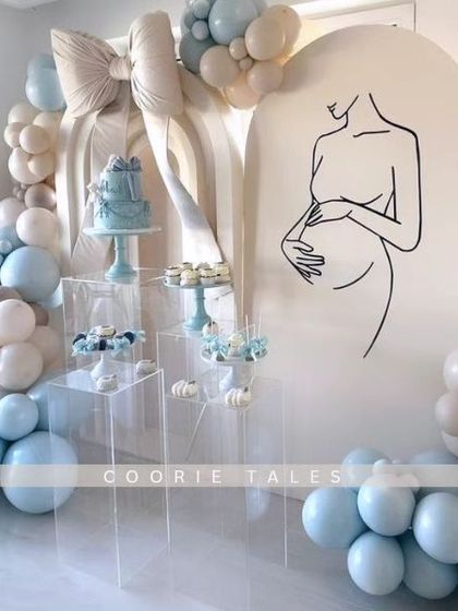 A modern and minimalist baby shower design. This elegant setup features a clean line-art illustration of a mother-to-be, clear acrylic dessert stands, and a soft blue and beige balloon arch for a truly chic celebration.