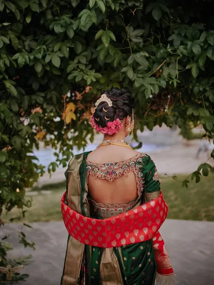 A detailed look at the back of this stunning bridal updo. The neatly tied bun, decorated with pink flowers, is a timeless choice that showcases the bride's jewelry and outfit beautifully.