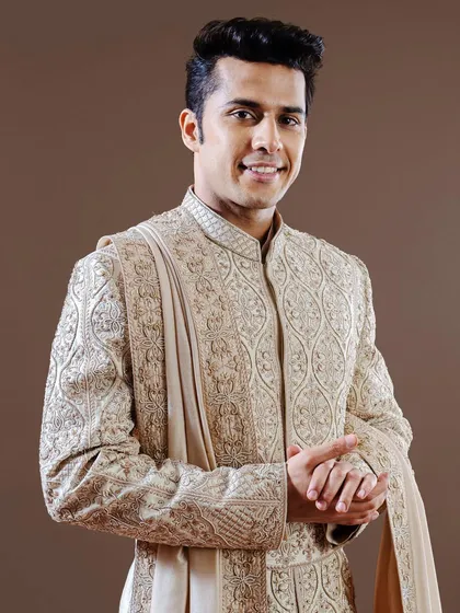 This golden-beige sherwani is a study in intricate craftsmanship, featuring dense, traditional embroidery. It is an ideal choice for the groom seeking a classic, opulent look for his wedding ceremony.