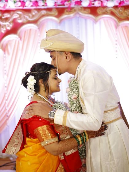 A sweet, intimate moment between the bride and groom. The bride's soft updo with fresh flowers is visible from the side.
