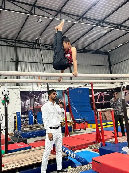 A coach provides instruction while a student holds a difficult position on the parallel bars. This level of personal attention ensures proper form and safety.