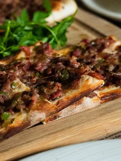 A Turkish lahmacun (flatbread with minced meat) served on a wooden board. The rustic presentation makes it look authentic and appealing.