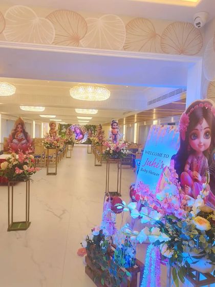 A view of the entire hall decorated for a Krishna-themed baby shower. The aisle is lined with floral stands and character cutouts, leading to the main stage.
