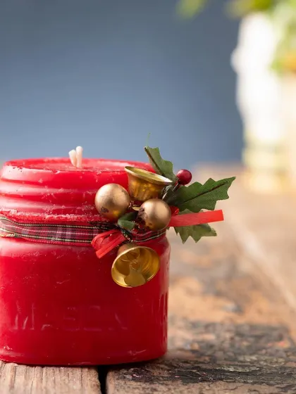A close-up of my red Christmas jar candle, decorated with a plaid ribbon, holly, and jingle bells.