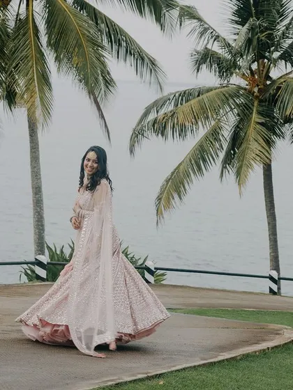 A joyful bridal portrait in a stunning destination. The bride's twirl shows off her beautiful pink lehenga against the backdrop of palm trees and the sea in Kerala, capturing a moment of pure happiness.