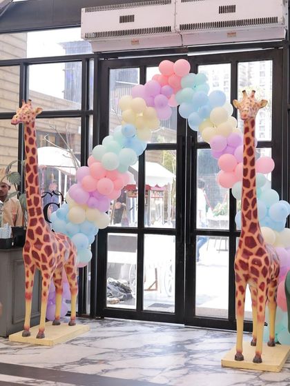 A grand entrance with two life-sized giraffe props and a pastel rainbow balloon arch. This setup immediately immerses guests in a whimsical and celebratory atmosphere.