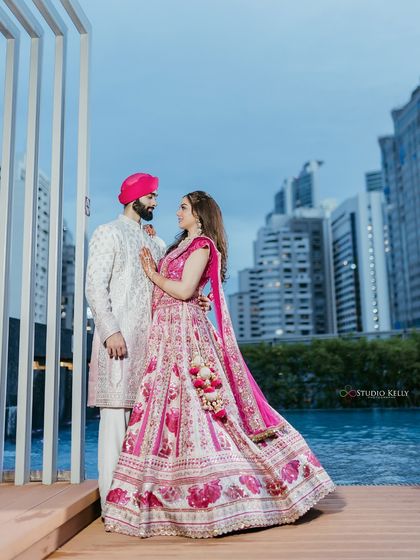 A dramatic portrait of the couple posing by a poolside against the Bangkok skyline at dusk, creating a glamorous and urban wedding photo.