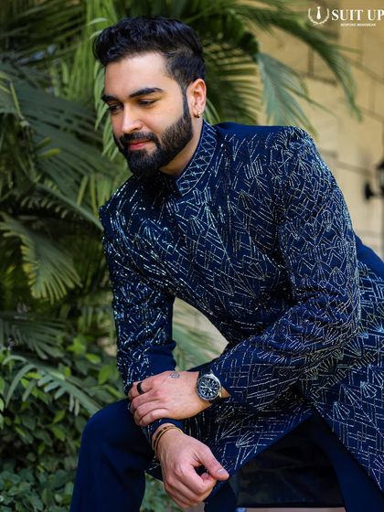 A client wearing a navy blue Indo-Western jacket with an intricate, textured pattern of silver embroidery. The look is luxurious and modern, perfect for a high-profile celebration.