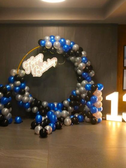 A stylish 13th birthday decoration for a boy. The setup features a blue, black, and silver balloon ring with large light-up marquee numbers.
