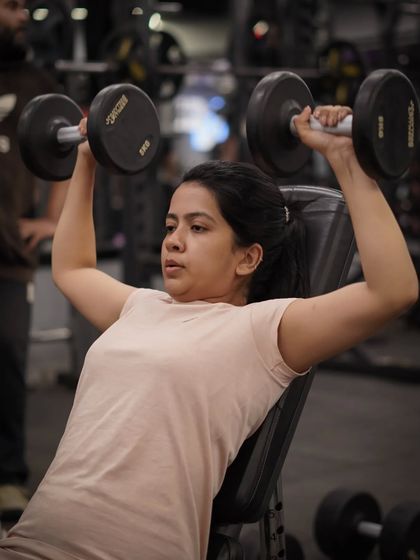 Using dumbbells for a seated shoulder press, this member is building strength and stability in her deltoid muscles.