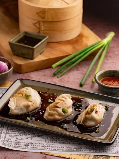 A plate of saucy Asian dumplings. The dark, glossy sauce and fresh garnish make the dish look incredibly flavorful.