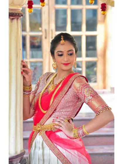 A beautiful moment captured in a custom half-saree lehenga. The outfit features a pink and silver blouse with intricate embroidery, paired with a white and red skirt, perfect for traditional ceremonies.