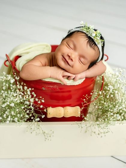 The sweetest smile from a baby resting in a bucket surrounded by delicate baby's breath. The combination of the red bucket and soft green wrap is simply lovely.