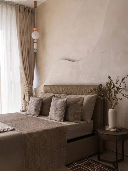 This bedroom showcases a beautiful, wave-like sculptural detail on the wall, adding a sense of gentle movement. The monochromatic brown and beige bedding creates a soothing, earthy atmosphere.