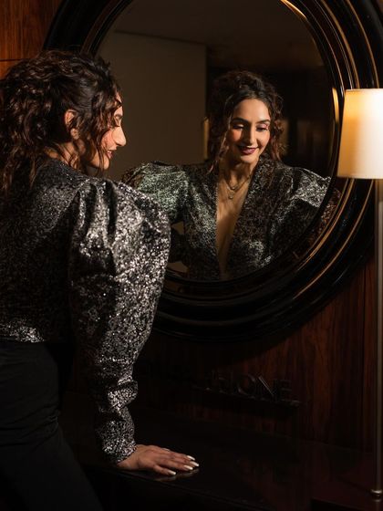 An interpretive shot using a mirror to create a reflective, layered portrait. The warm, low-key lighting adds a touch of mystery and sophistication to this indoor shoot.