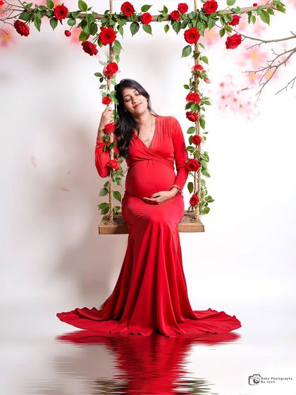 A beautiful solo shot on a floral swing with a water reflection effect. The mom-to-be's red gown stands out against the simple background, creating a striking image.
