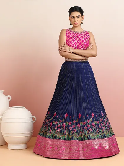 A striking navy blue pleated silk lehenga with a rising floral motif, paired with a vibrant pink embroidered blouse. The color contrast is bold and beautiful.