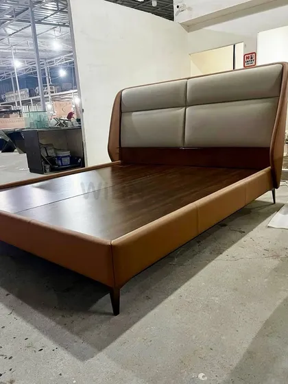 A glimpse from our factory of a custom luxury bed. This piece features a sleek frame in tan leather with a contrasting cream-colored padded headboard.