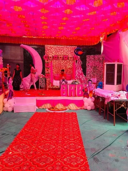 A baby shower pandal with a long red carpet entrance, leading to a beautifully decorated stage with a moon prop and swing.