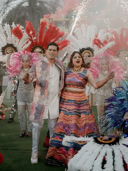 A joyous shot of the couple at their carnival, surrounded by performers. The colorful feathers and pyrotechnics add to the celebratory atmosphere.