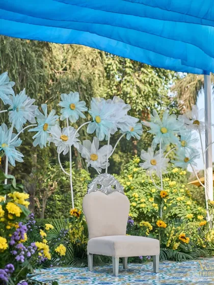 The bride's seat for the Haldi ceremony, set against a backdrop of oversized, handcrafted paper daisies and a field of real sunflowers.