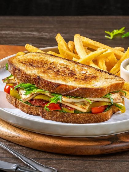 A grilled halloumi and vegetable sandwich on sourdough bread, served with fries for a hearty cafe meal.