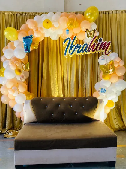 This is a personalized setup for a naming ceremony, or Naamkaran. We created a full circular balloon arch in soft peach and white tones and added a custom name sign for "Ibrahim" to make the occasion truly special.