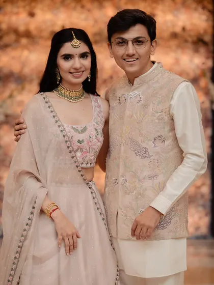 A happy portrait of the couple. Their coordinated pastel outfits and the soft floral background create a look of effortless elegance, perfect for a daytime engagement or reception.