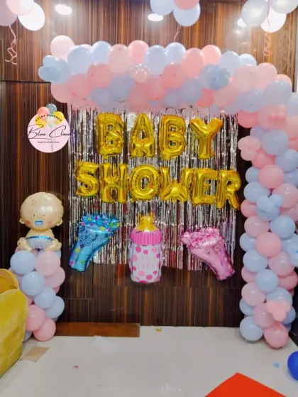 A gender-neutral baby shower decoration with a pink and blue balloon arch over a silver shimmer curtain.