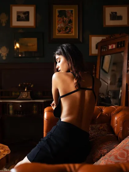 A moody and atmospheric shot focusing on the model's back and the vintage-inspired room. The composition creates a sense of mystery and introspection.