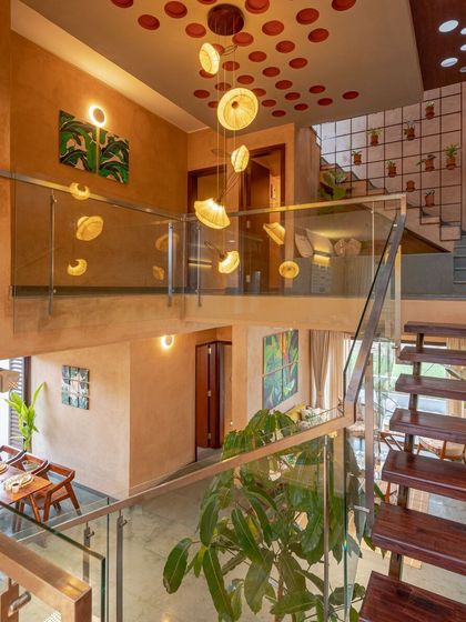 A view from the upper level looking down into the double-height atrium. Custom light fixtures made from banana leaves hang like delicate sculptures, while the glass railing ensures an unobstructed view and a sense of openness.
