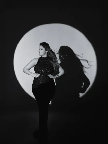 A dramatic black and white portrait using a spotlight to create a striking silhouette and shadow. This artistic approach focuses on form, movement, and the powerful presence of the mother-to-be.