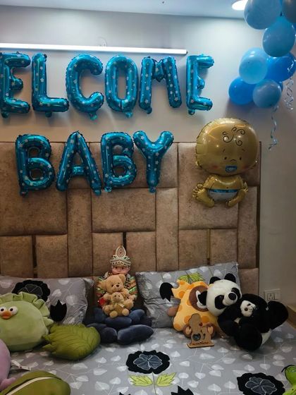 A bedroom decorated for a new baby's arrival, with "Welcome Baby" foil balloons and the bed filled with soft toys.