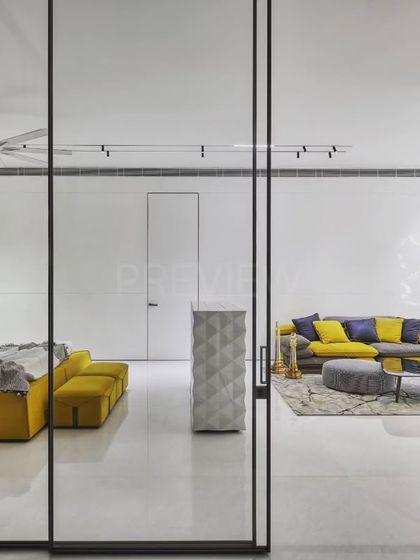 This view shows the connection between the vibrant bedroom and an adjacent living space, separated by a minimalist glass partition. The design maintains an open, airy feel while defining distinct functional zones.