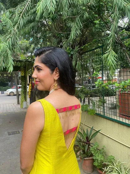 A desi touch for a modern gown. This custom raw silk gown in a vibrant yellow features a traditional Banarasi border and a daring deep-V back with tassel detailing, making it a perfect outfit for a reception or cocktail evening.