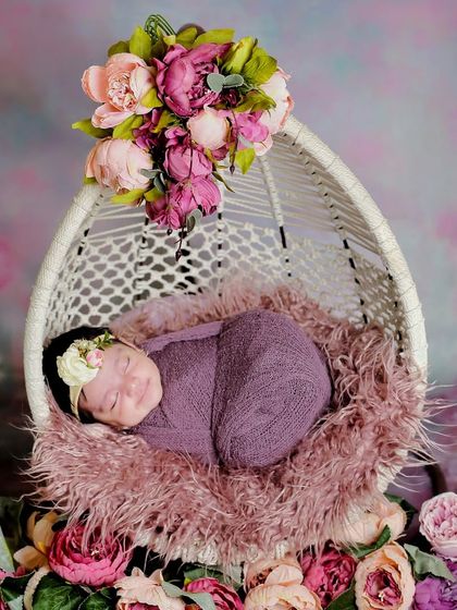 A beautiful floral theme, with a newborn sleeping peacefully in a hanging egg chair surrounded by pink and purple peonies. This setup is perfect for a dreamy, feminine portrait.