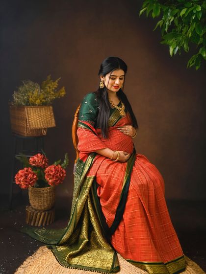 A serene, seated portrait capturing the grace of the expectant mother. The earthy tones of the background complement the traditional saree perfectly.