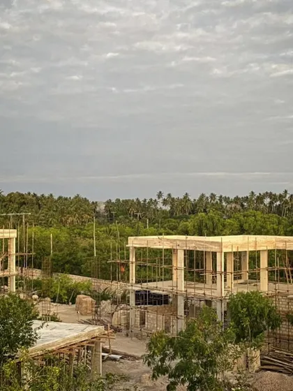 An overview of the phase two construction site under a cloudy sky. The raw concrete frames stand ready for the next stage of work, surrounded by the dense green landscape of Zanzibar.