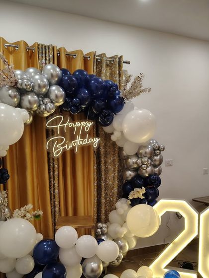 This 26th birthday decoration features a modern color scheme of navy blue, white, and silver. The balloon ring is set against a gold curtain for extra glamour.