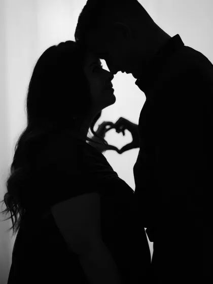 Sometimes the most powerful moments are the quietest. This artistic silhouette shot captures the intimate connection between expecting parents, with their hands forming a heart in the background, symbolizing the love that started it all.