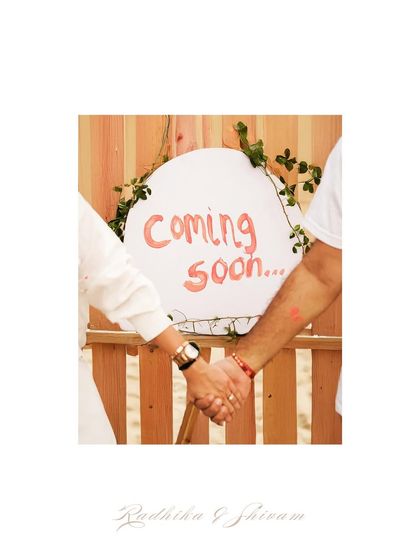 A close-up of the couple holding hands behind their "Coming Soon" sign, a sweet detail from their beach announcement.